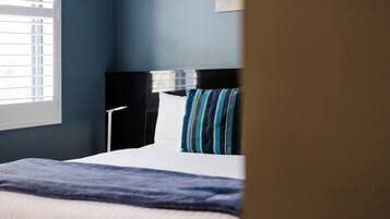 A hotel room with a bed, a nightstand, a lamp, and a window with blinds.