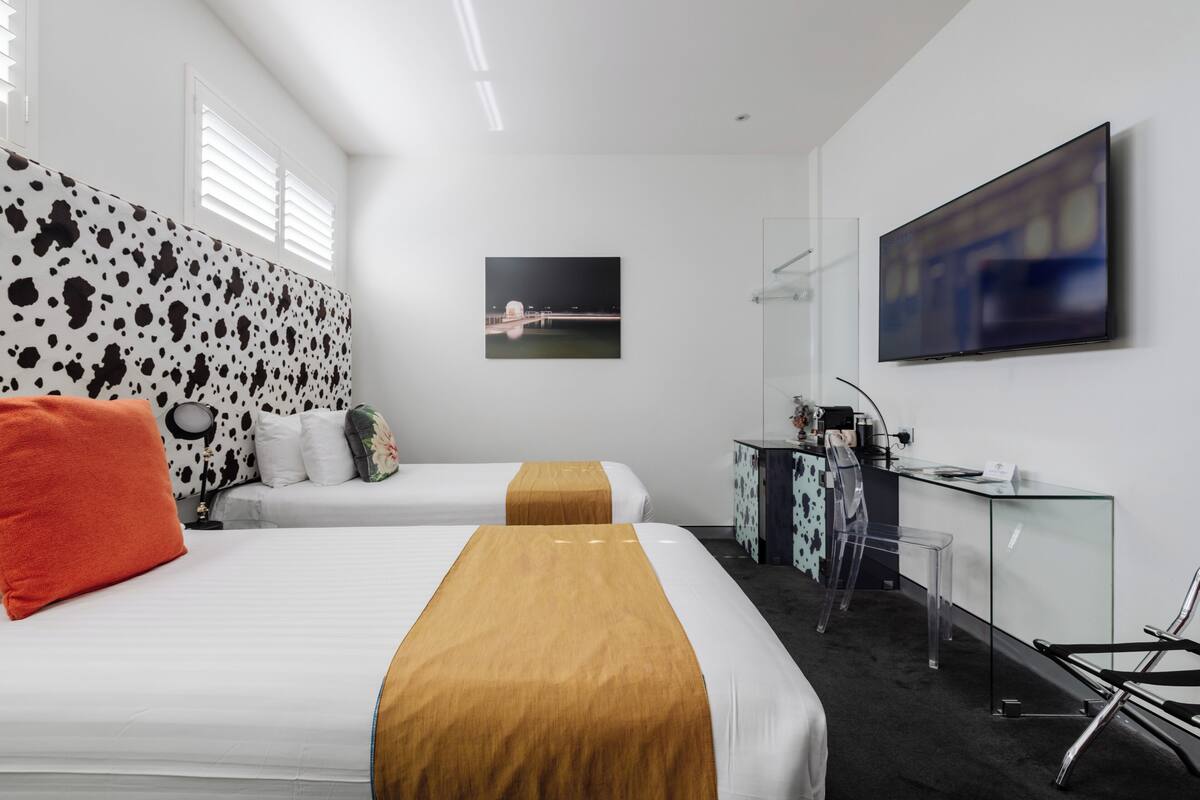 A hotel room with two beds, a desk, a chair, a TV, and a picture on the wall.