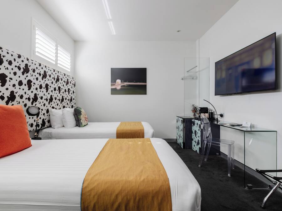 Een hotelkamer met twee bedden, een bureau, een stoel, een televisie en een schilderij aan de muur.