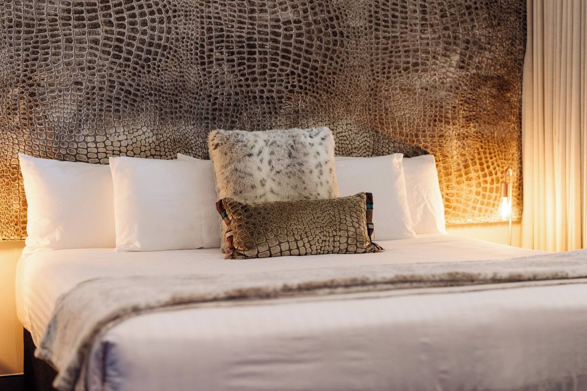 A bed with white linens, a textured headboard, and a single decorative pillow.