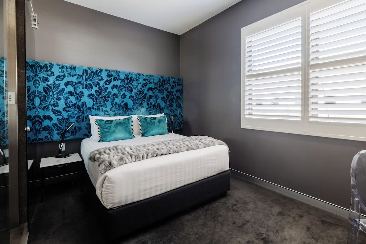 A bedroom with a bed, nightstand, lamp, and window with blinds.