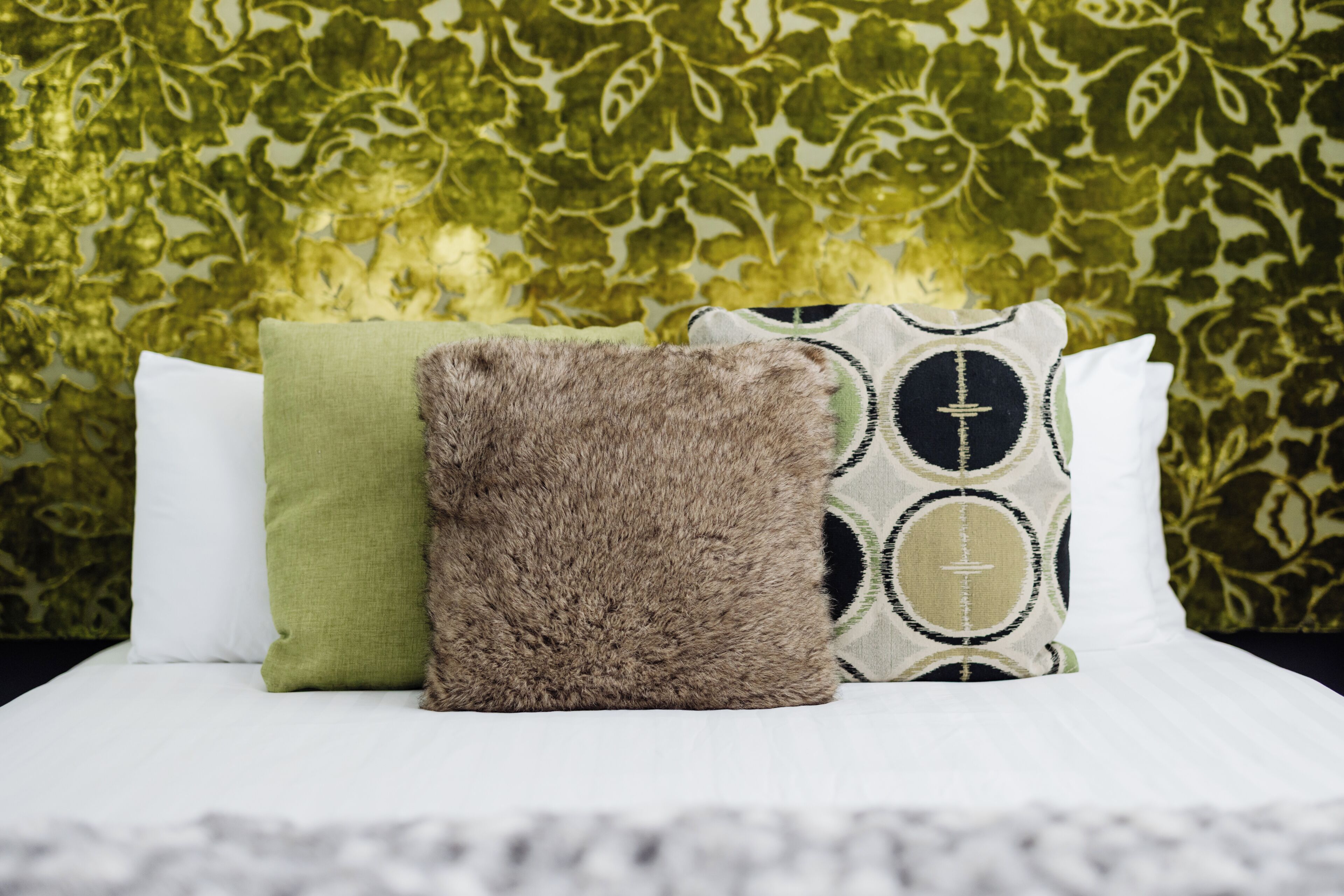 A bed with three pillows and a patterned wall.