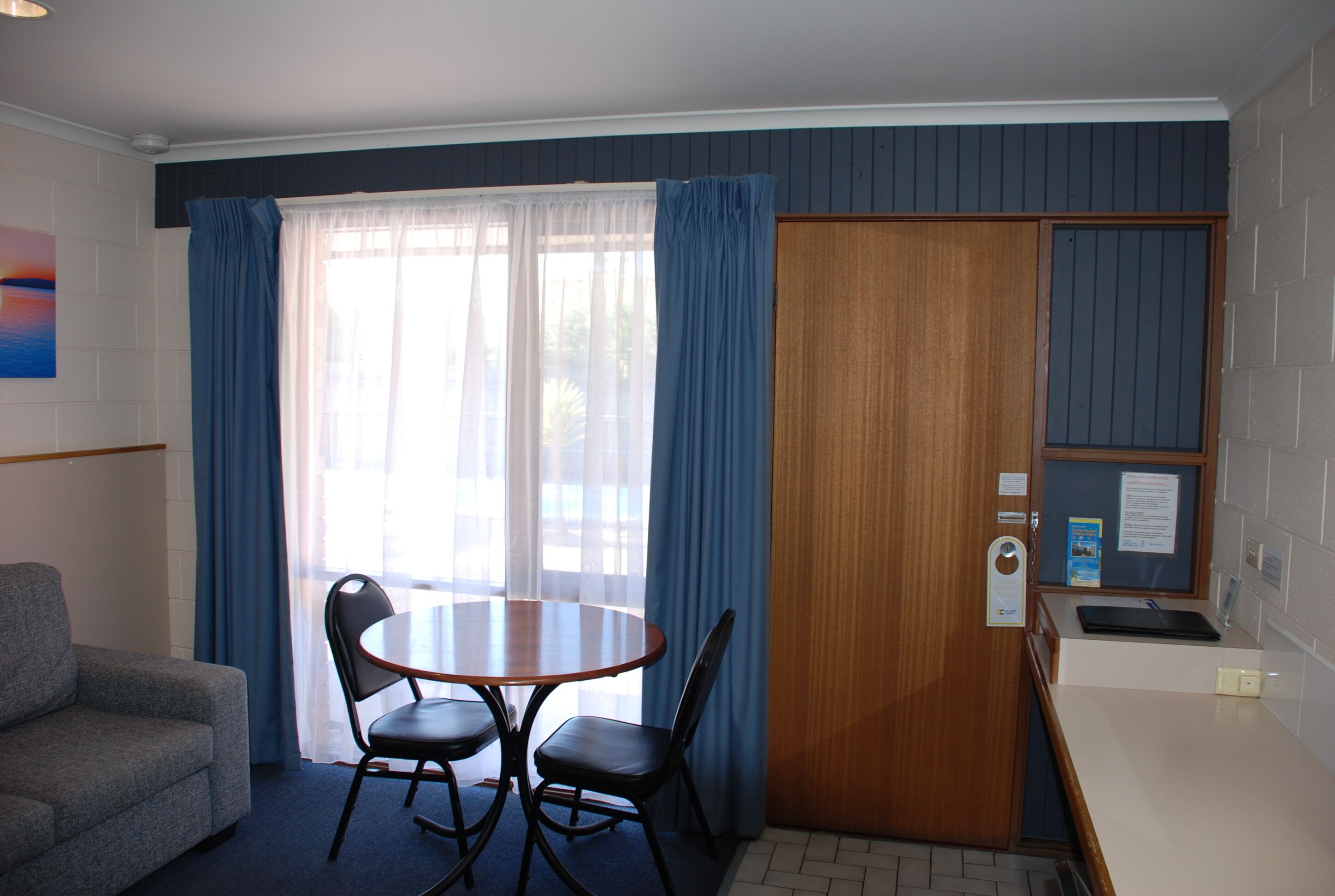 Ett litet, kompakt rum med ett runt bord och två stolar, en soffa, en trädörr och en liten köksdel.