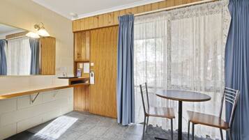 A compact kitchen with a wooden countertop, a sink, and a mirror. There is a round table with two chairs and a window with lace curtains.