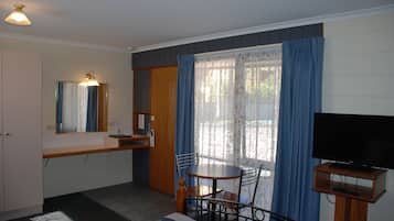 Une petite pièce bien éclairée, avec une table et des chaises, un téléviseur posé sur un meuble, un miroir et une fenêtre avec des rideaux.