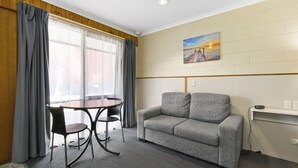 A hotel room with a gray sofa, a round table with chairs, and a painting on the wall. - Cunningham Shore Motel (Lakes Entrance)
