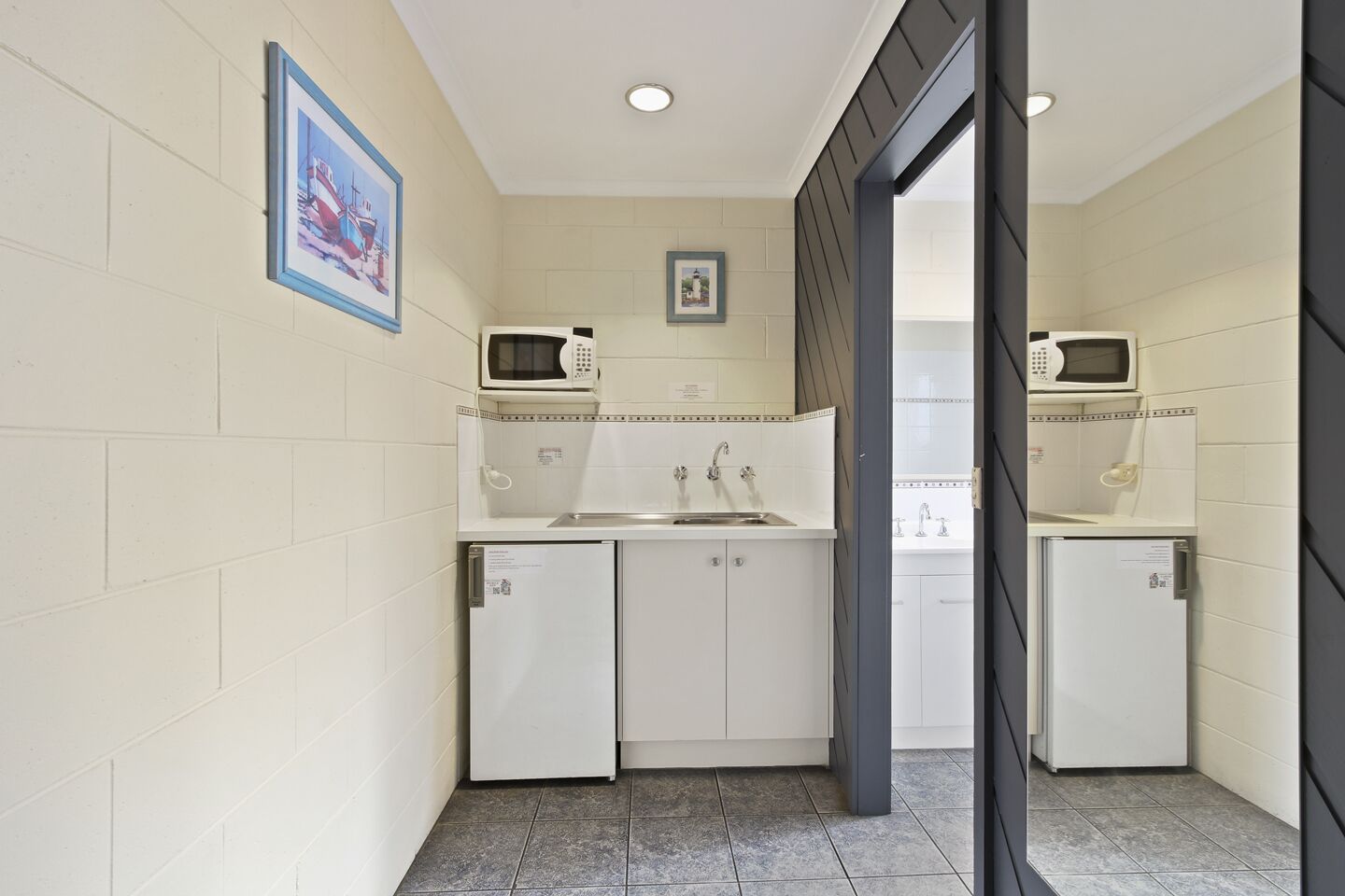 A compact kitchen with white cabinets, a sink, and two microwaves.