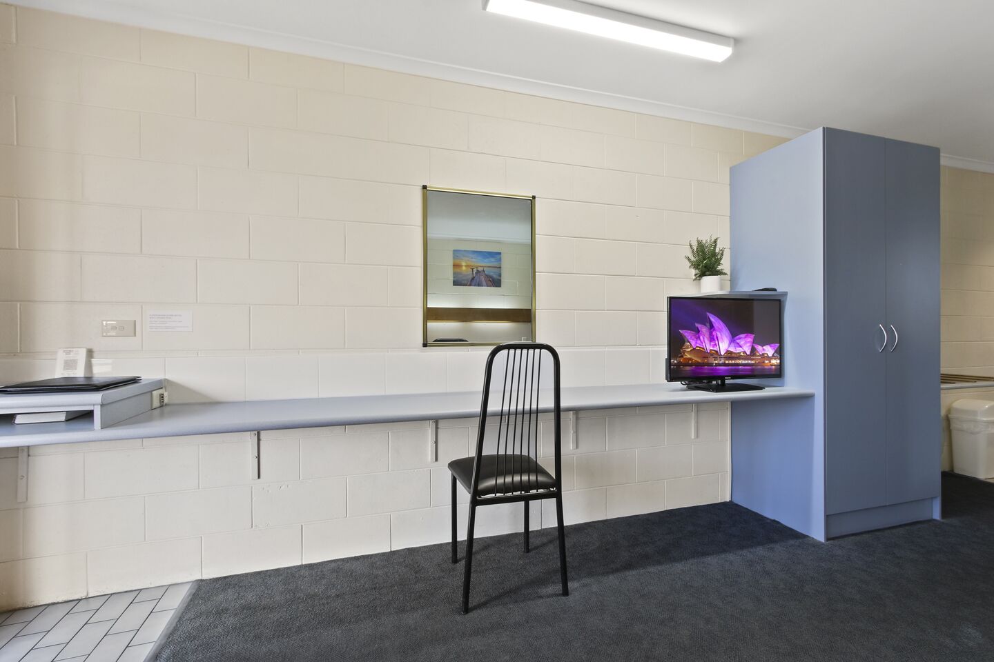 A reception area with a counter, a chair, a television displaying a cityscape, a framed picture on the wall, and a grey cabinet.