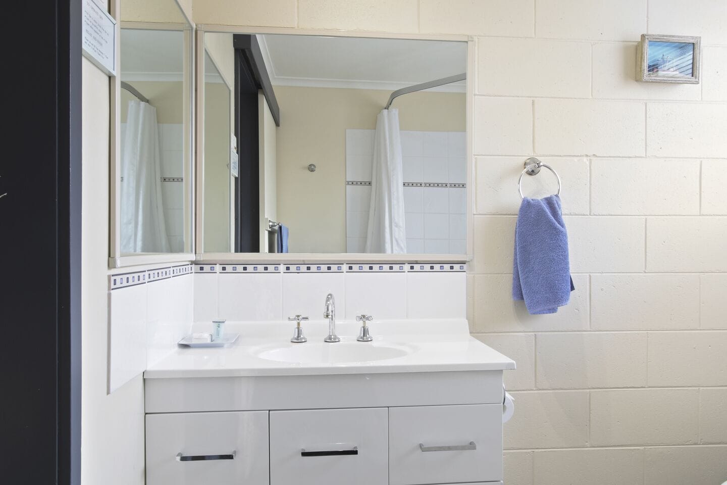 Casa de banho com lavatório branco, duas torneiras, espelho e porta-toalhas com uma toalha azul.