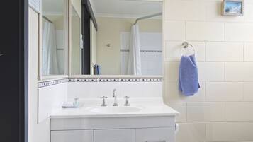 Casa de banho com lavatório branco, duas torneiras, espelho e porta-toalhas com uma toalha azul.