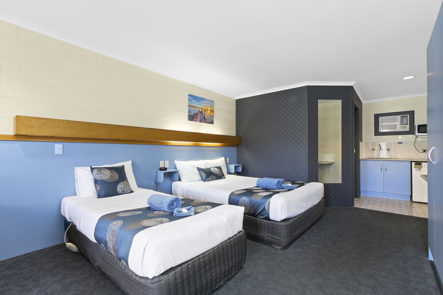 Ein Hotelzimmer mit zwei Betten, einer kleinen Küchenzeile und einem durchgegangenen Tür erkennbaren Badezimmer.