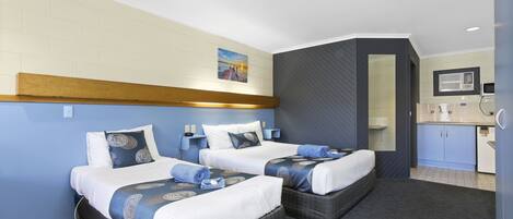 A hotel room with two beds, a small kitchenette, and a bathroom visible through an open door.