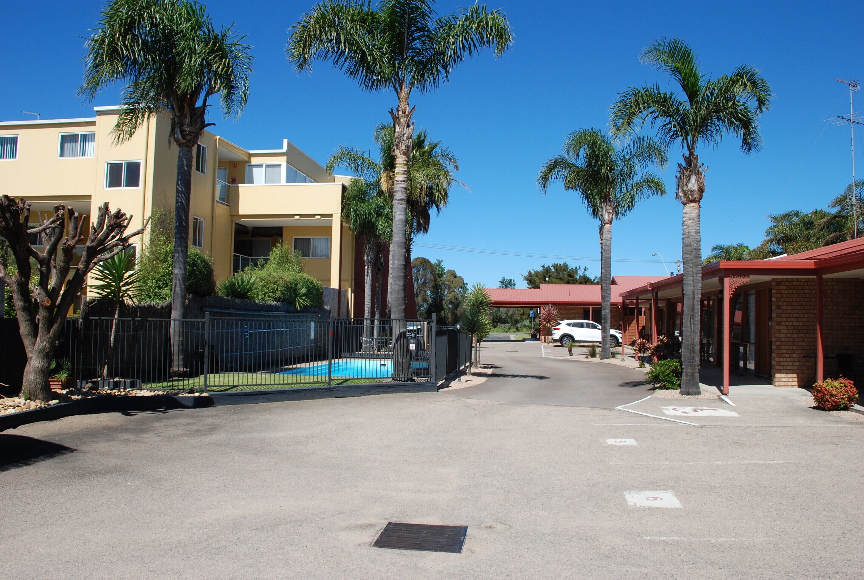Une vue de rue avec une piscine, des palmiers et un bâtiment doté d’un toit rouge.