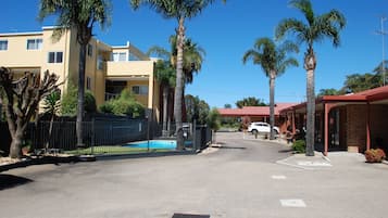 Une vue de rue avec une piscine, des palmiers et un bâtiment doté d’un toit rouge.