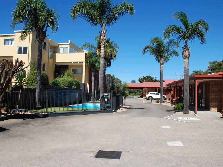 Une vue de rue avec une piscine, des palmiers et un bâtiment doté d’un toit rouge.