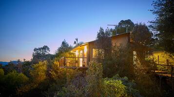 Una casa moderna con balcón de vidrio, rodeada de vegetación densa.