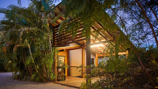 A modern wooden structure with a covered entrance, surrounded by dense tropical vegetation. - Dayboro Cottages (King Scrub)