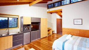 A compact kitchen with a microwave, stove, and sink, wooden cabinets, and a window overlooking greenery. - Dayboro Cottages (King Scrub)