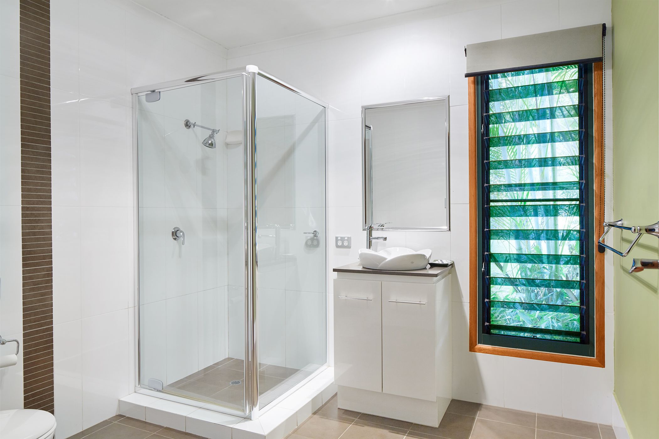 Une salle de bain moderne avec une douche en verre, un lavabo avec un miroir et une fenêtre avec des stores.