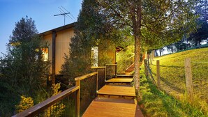 A wooden deck leading to a building with a metal fence and trees. - Dayboro Cottages (King Scrub)