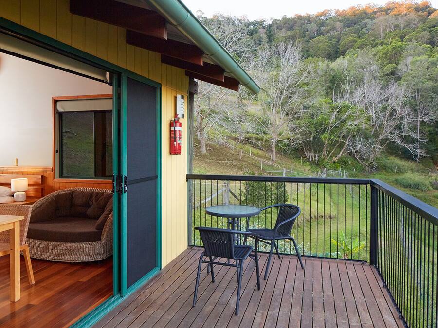 Un balcón con terraza de madera, un sofá de mimbre, dos sillones y una mesa.