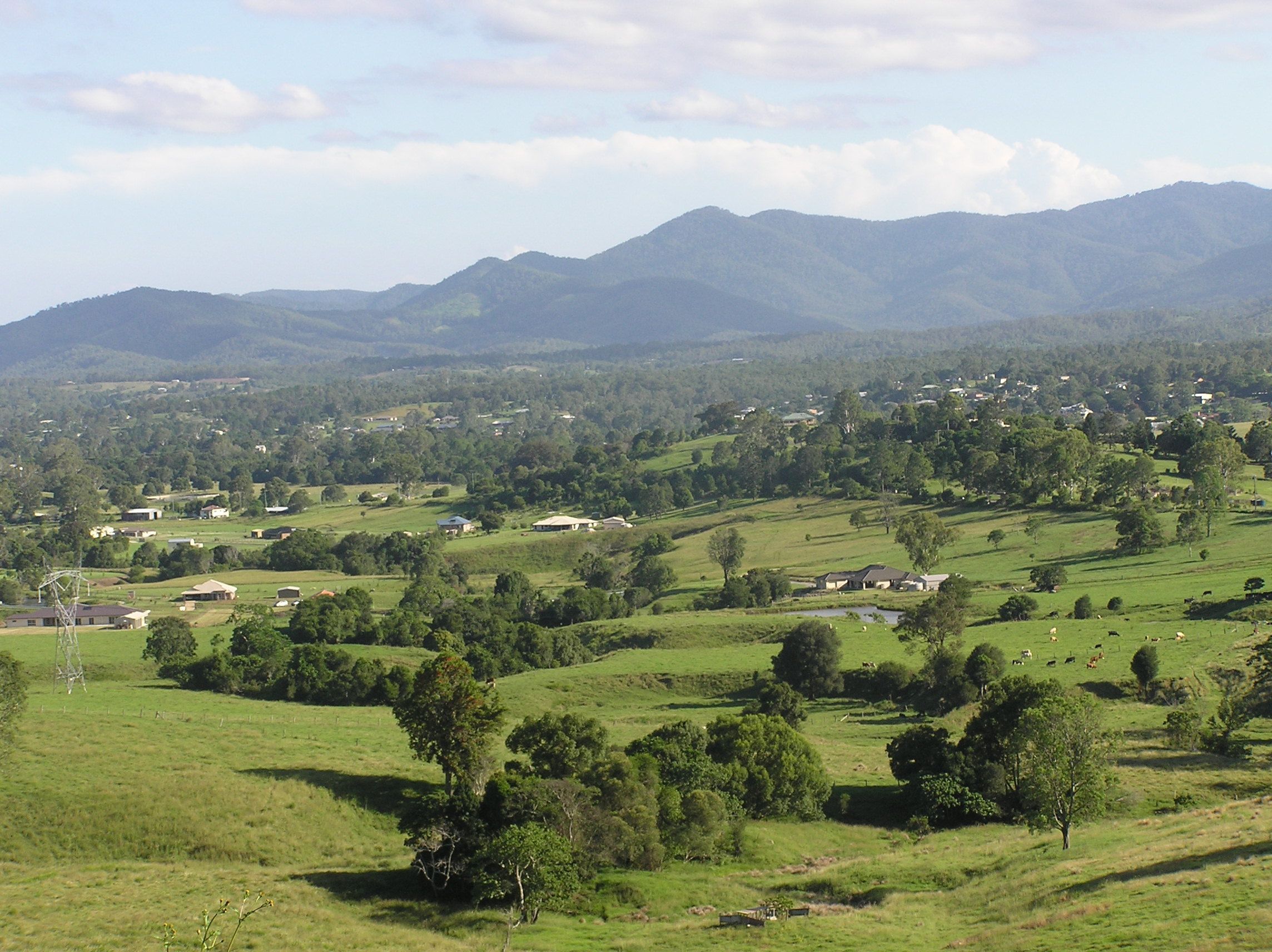 Ländliche Landschaft mit sanften Hügeln, verstreuten Häusern und einem Bergpanorama im Hintergrund.