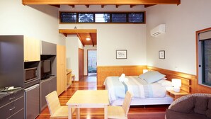 A compact hotel room with a bed, a small table, a chair, a kitchenette, and a large window. - Dayboro Cottages (King Scrub)