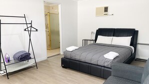 A modern bedroom with a bed, a hanging clothes rack, a small table, and a grey sofa.