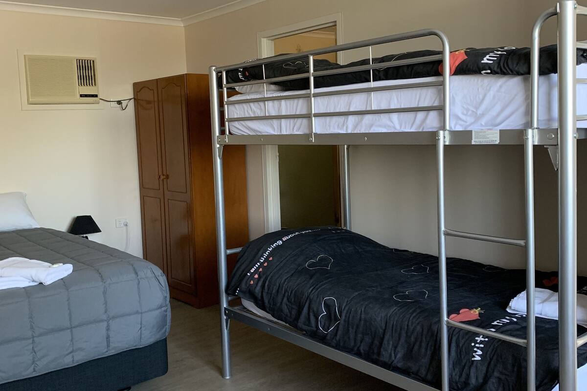 Een slaapkamer met een stapelbed, een grijze bed, een kledingkast en een plafondlamp.