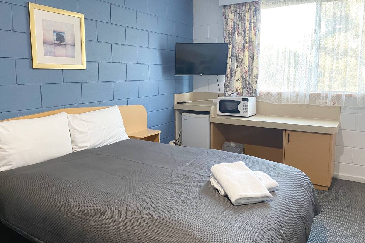 Een hotelkamer met een bed, een bureau met een magnetron, een televisie en een raam met gordijnen.