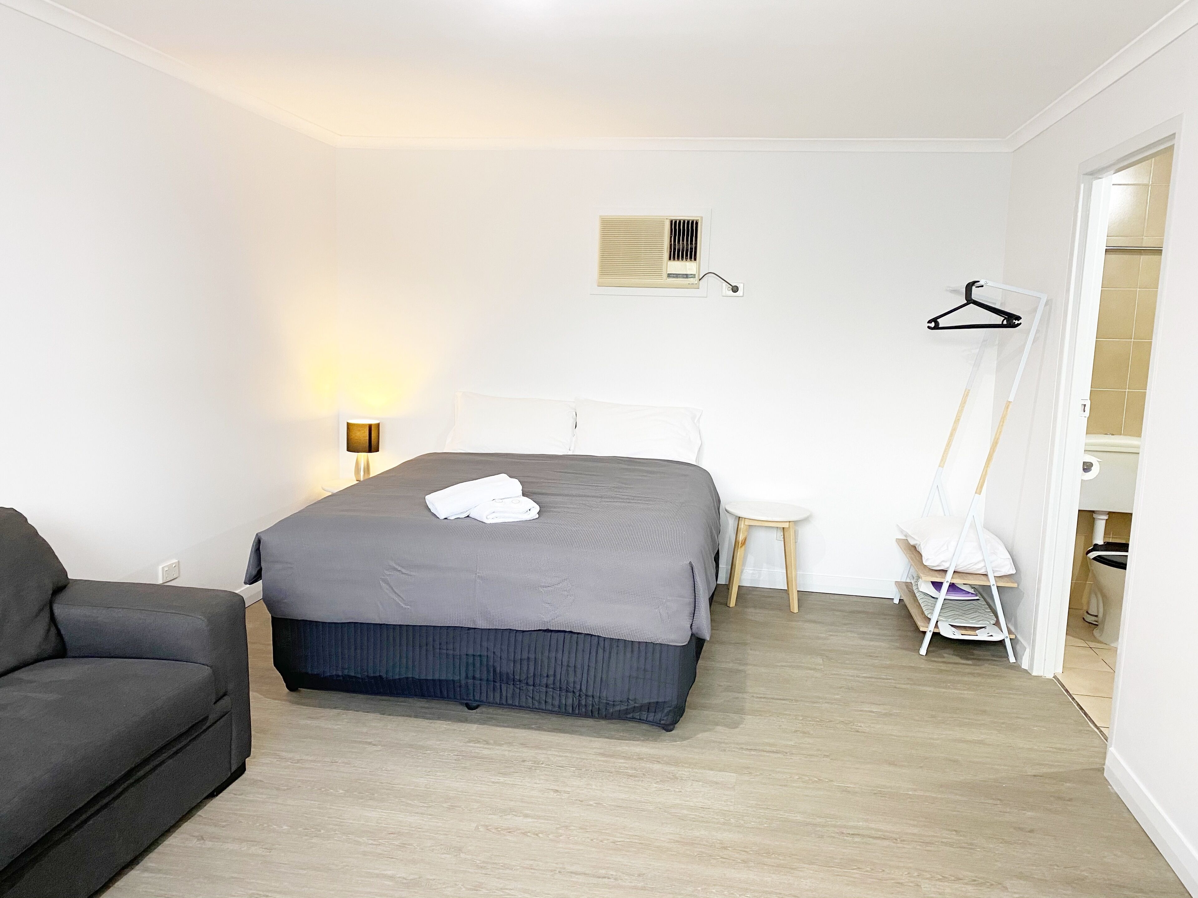 Une chambre d’hôtel bien rangée, avec un lit, une table de chevet, une lampe, une chaise et une armoire.
