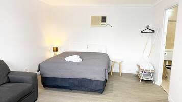 Une chambre d’hôtel bien rangée, avec un lit, une table de chevet, une lampe, une chaise et une armoire.