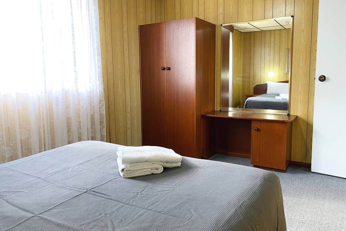 Een hotelkamer met een bed, een houten garderobe, een spiegel en een klein bureau.