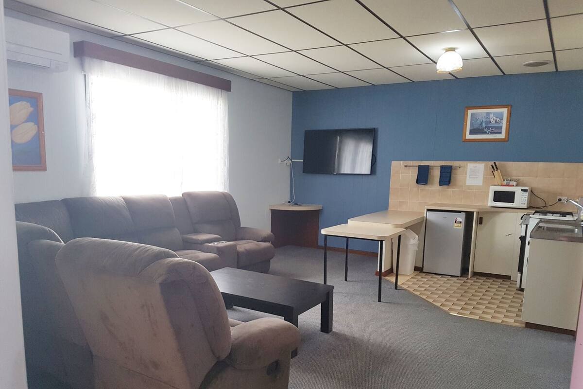Een ruimtelijk ingerichte leefruimte met een bank, een kleine tafel, een televisie en een kitchenette.