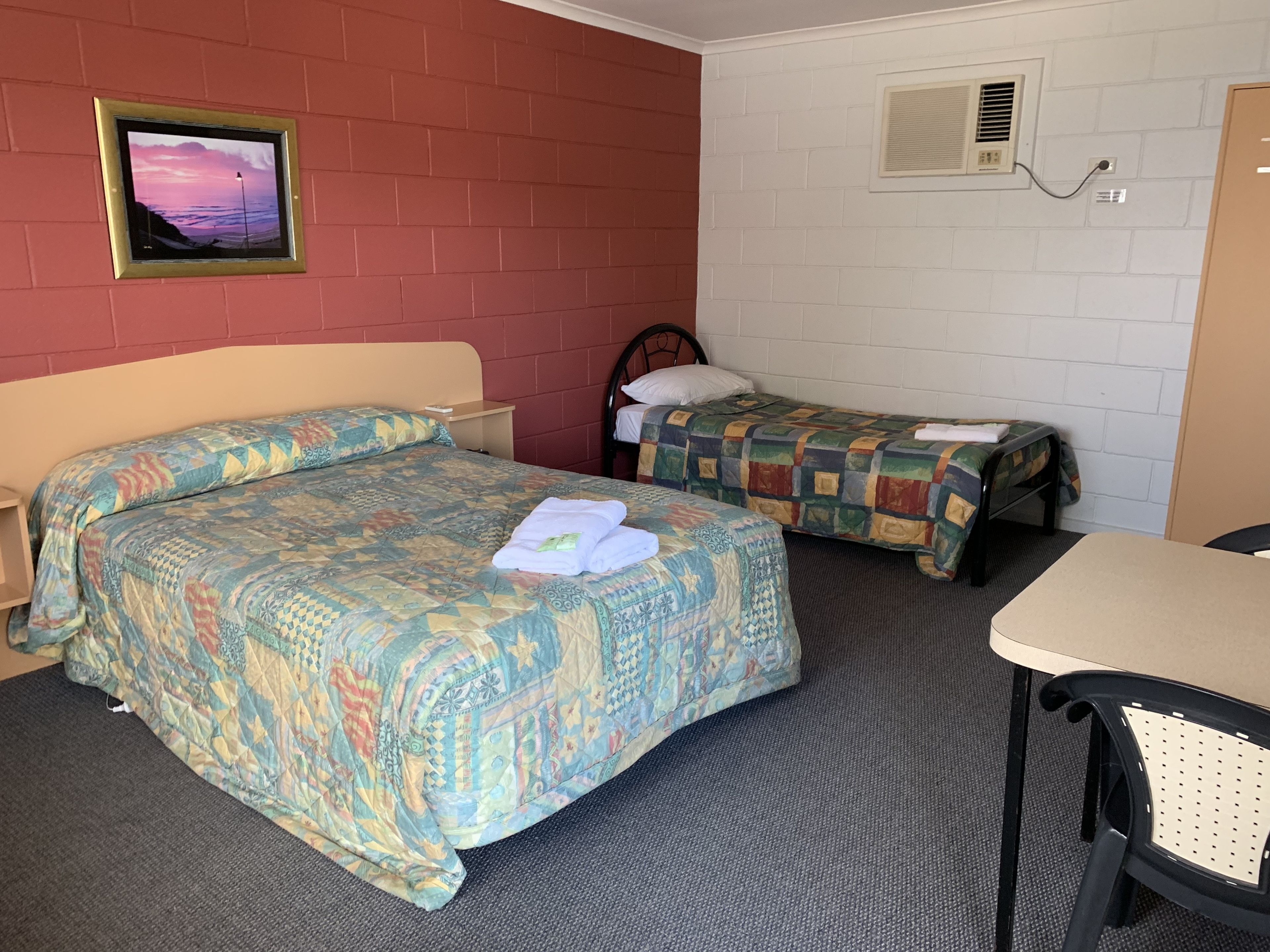 A hotel room with two beds, a desk, a chair, and a picture on the wall.