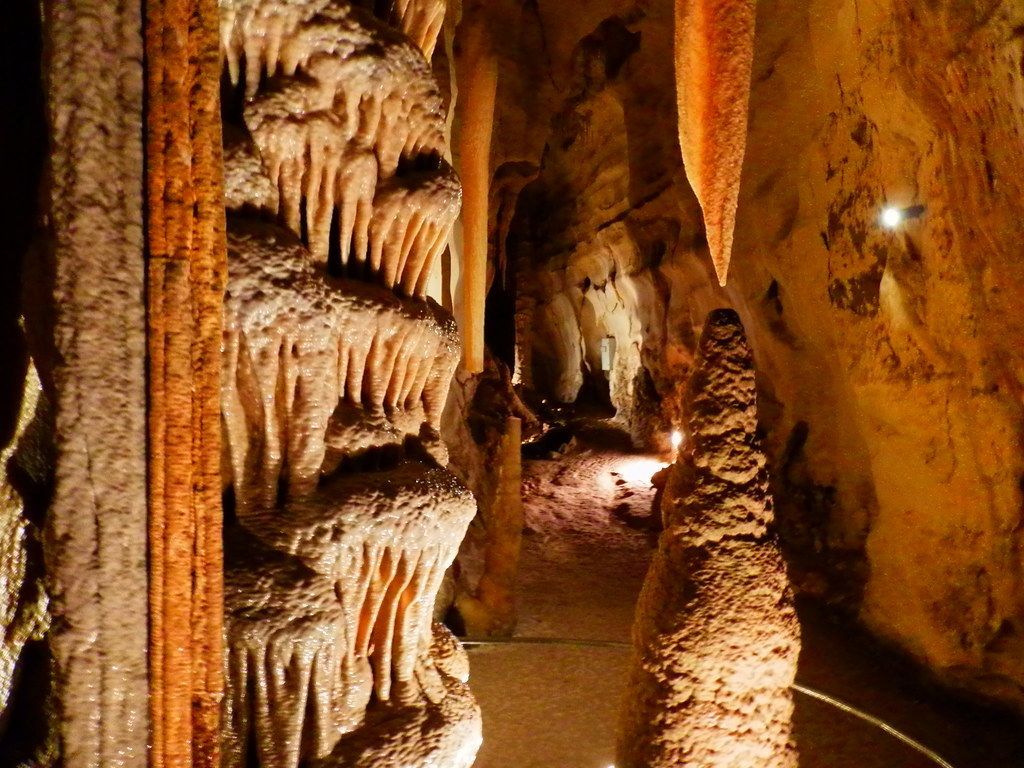 Una cueva con estalactitas y estalagmitas, iluminada con luz artificial.