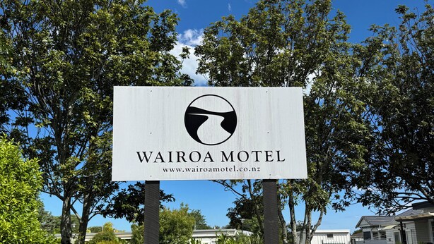 A sign for Wairoa Motel with a website URL, set against a backdrop of trees and a clear sky.