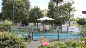 A swimming pool surrounded by a fence, with lounge chairs and an umbrella.