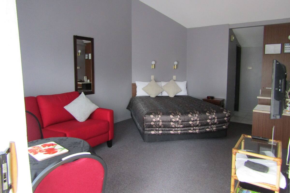 A hotel room with a bed, a red sofa, a small table, and a TV.
