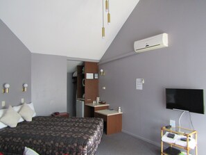 A hotel room with a bed, a desk, a TV, and an air conditioning unit. - Gateway Motor Lodge (Dannevirke)
