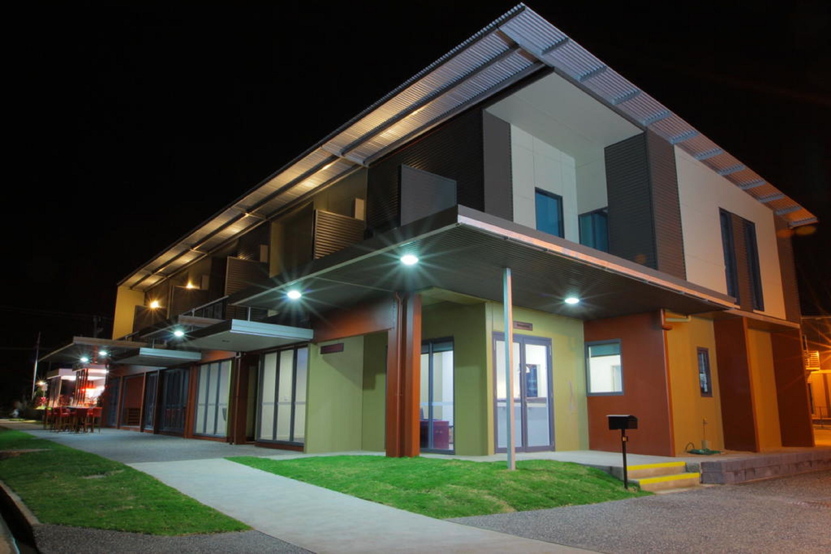 Un edificio moderno de varios pisos con techo plano, grandes ventanales e iluminación exterior nocturna.