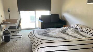 Ett hotellrum med en säng, ett skrivbord, en stol, en takfläkt och ett fönster med utsikt.