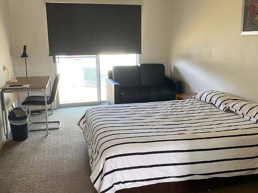 Ett hotellrum med en säng, ett skrivbord, en stol, en takfläkt och ett fönster med utsikt.