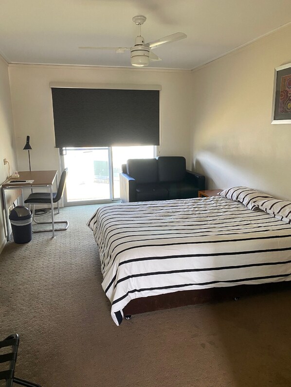 A hotel room with a bed, a desk, a chair, a ceiling fan, and a window with a view. - Black Rock Inn (Blackwater)