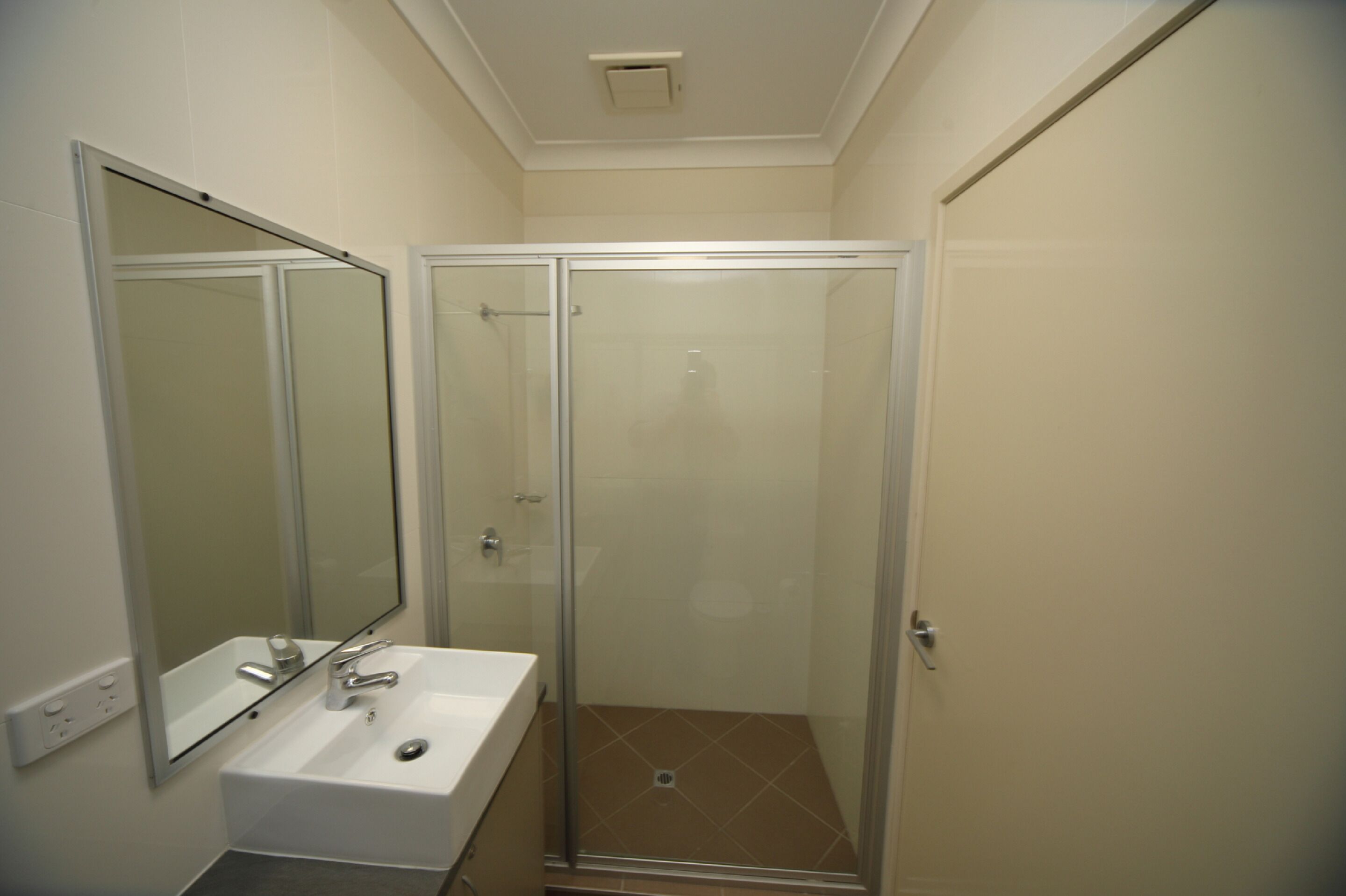 A bathroom with a glass-enclosed shower, a white sink, and a mirror.