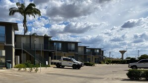 A parking lot with a modern building featuring a staircase and a palm tree. - Black Rock Inn (Blackwater)