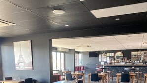 A spacious indoor area with multiple tables and chairs, a bar area with a variety of bottles, and a large window providing natural light. - Black Rock Inn (Blackwater)