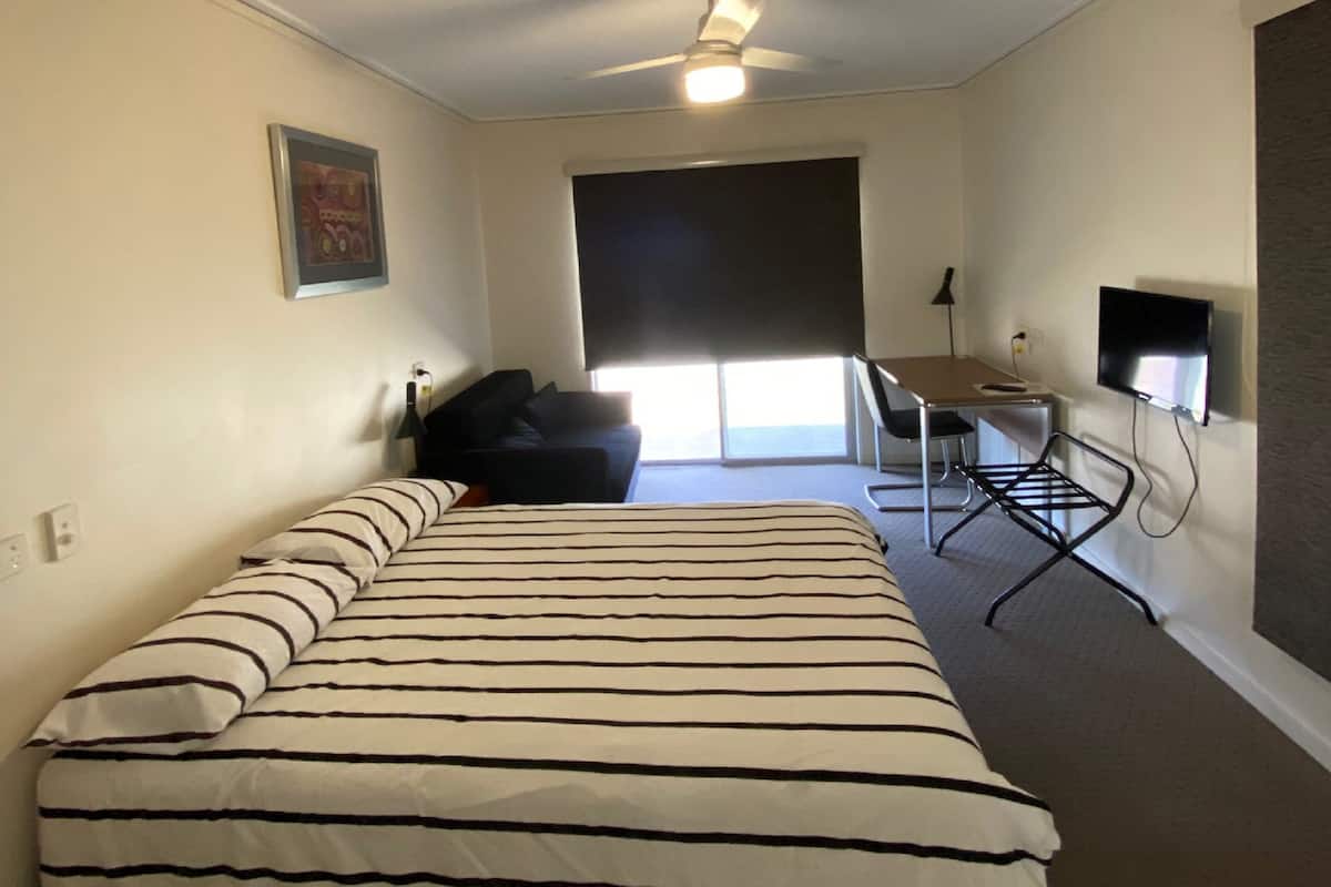 Ein Schlafzimmer mit Bett, Schreibtisch, Stuhl, Fernseher und Deckenventilator.