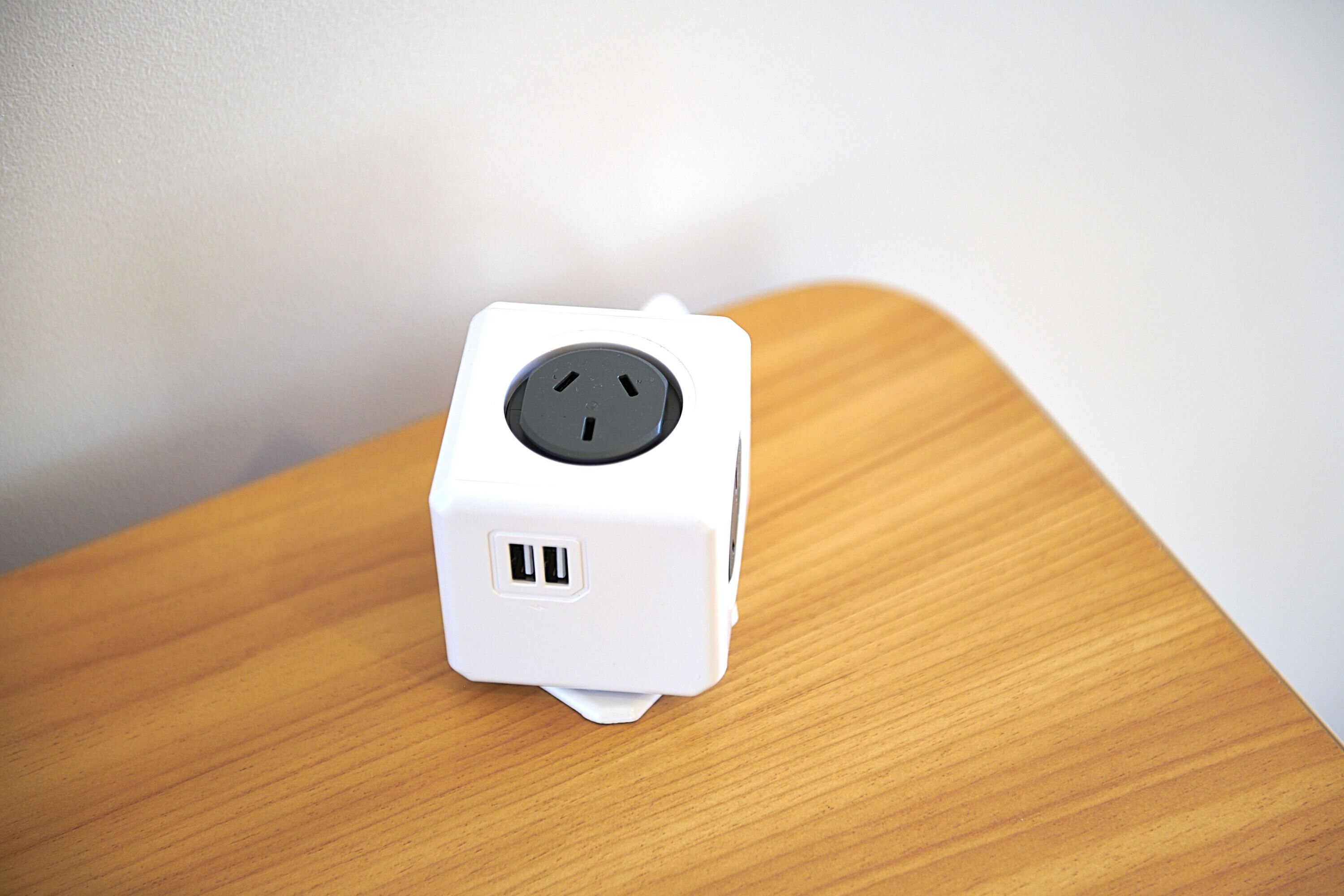 A white power strip with two USB ports and a three-prong plug on a wooden surface.