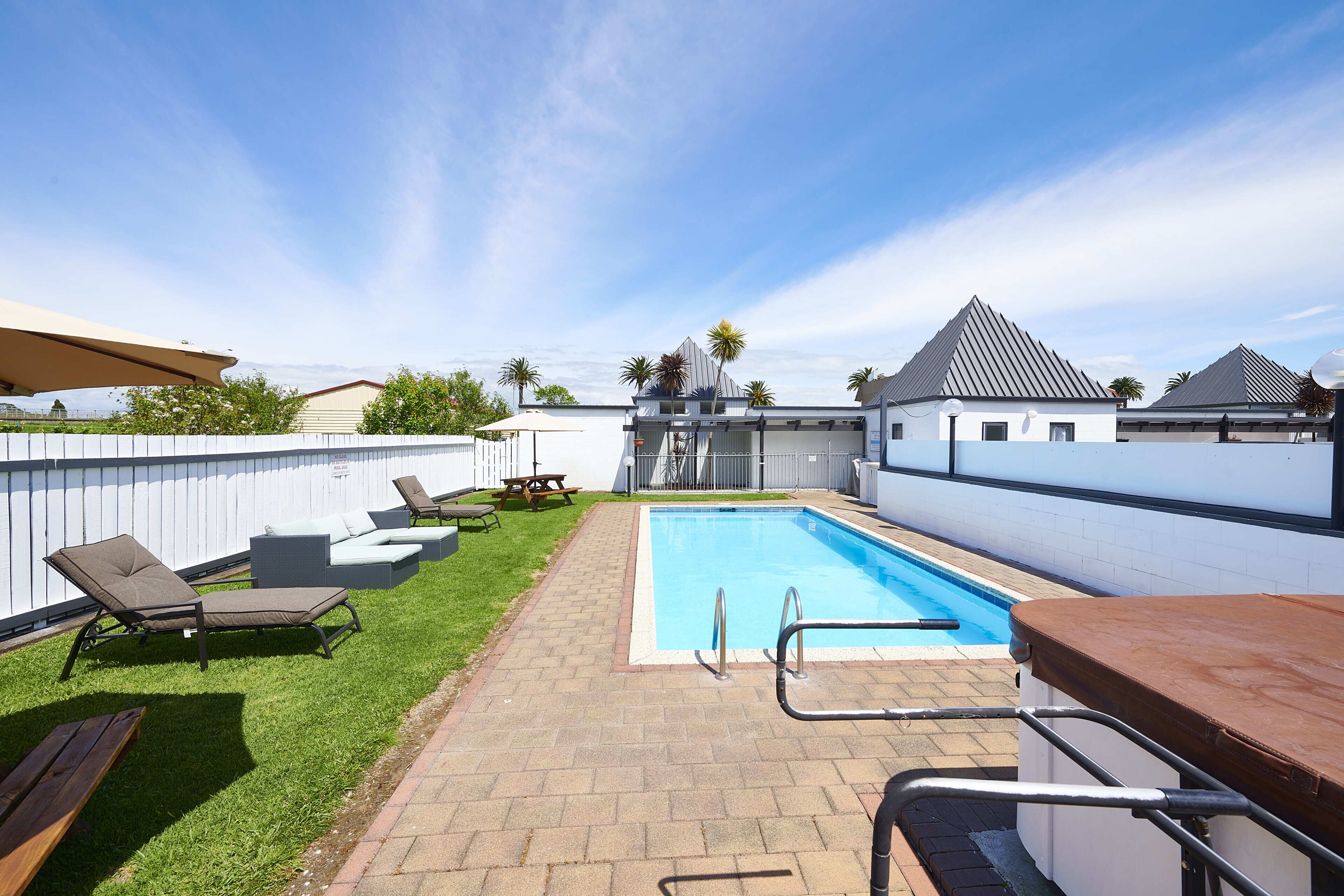 A backyard with a swimming pool, lounge chairs, and a barbecue area.